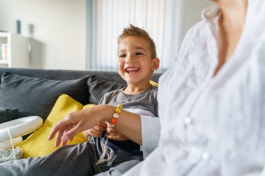 Evinde annesinin gülümseyen küçük beyaz bir çocuğun portresi - yaz günü kanepede gülen küçük bir çocuk - 4 yaşındaki mutlu çocuk belini kaldırsın - çocukluk mutluluğu ve neşe kavramı
