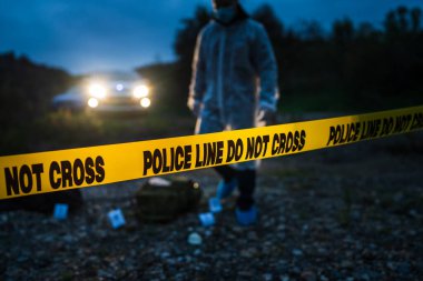 Forensic police investigator collecting evidence at the crime scene by the river in nature at night selective focus on police line tape clipart