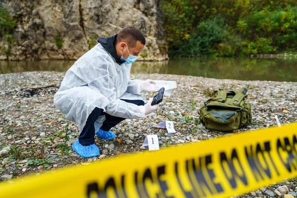 法医调查员手持枪在自然河边的犯罪现场收集证据 — 图库照片