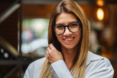 Beyaz gömlek ve gözlük takmış güzel beyaz bir kadının kameraya bakıp fotokopi çekerken gerçek insanların gülümsediği ön manzara.