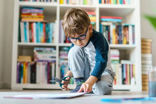 家の床で遊ぶ4歳の白人の少年の正面図 紙の教育を削減するはさみを使用して小さな子供概念を成長させる芸術スキルを開発 — ストック写真