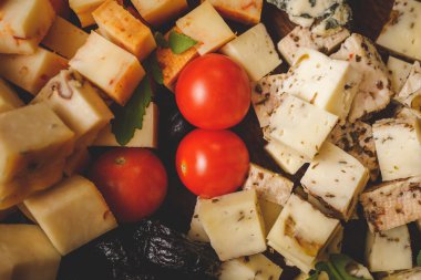 Kurulda çeşitli peynir dilimleri ve kiraz domatesleri var.