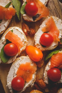 Ekmek ve krem peynirli sandviç dilimlerinde kurutulmuş füme somon. Kiraz domatesli ve roket salatalı.