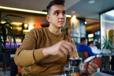 Kafe 'de tek başına oturan beyaz bir adam elinde çay fotokopisi olan mutlu bir erkeği görüyor.