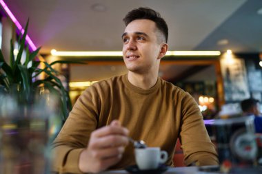 Kafeteryada tek başına oturan beyaz bir adam elinde bir fincan kahve fotokopi alanı tutan mutlu bir erkeği görüyor.