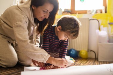 Anne ve oğlu evde oynayıp kağıt keserken makas ve sanat oyuncakları yaparken eğleniyorlar. Yetenekler geliştiriyorlar. Çocukluk ve gelişim, aile eğlencesi kavramı.
