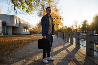 Sonbahar günü elinde iş çantasıyla duran beyaz bir adamın ön görüntüsü. Gerçek insanlar. Genç işadamı işe ilk gününde ya da işten sonra üzgün ve yorgun düşünüyor.