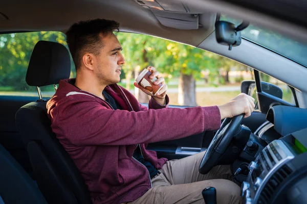 車のコピースペースで運転中や待機中にテイクアウトコーヒーを飲んでいる若い白人男性の側面図 — ストック写真