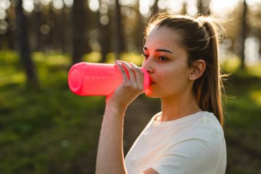Doğanın ormanlarında, elinde bir şişe su tutarak fren yapan ve doğanın fotokopi alanında dinlenme eğitimi alan beyaz bir kadının yarı uzunluğunda ön manzara.