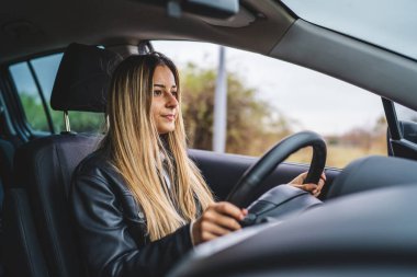 Genç bir yetişkin, beyaz bir kadın direksiyon başında beklerken yol kenarına bakıyor kadın sürücü yer kopyalıyor gerçek insanlar trafik sıkışıklığı yaşıyor