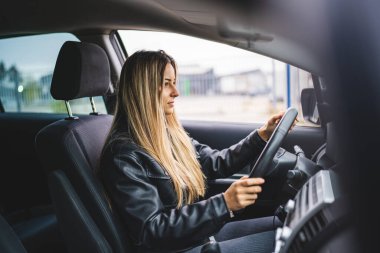Genç bir yetişkin, beyaz bir kadın direksiyon başında beklerken yol kenarına bakıyor. Kadın sürücü, gerçek insanları taklit ediyor.