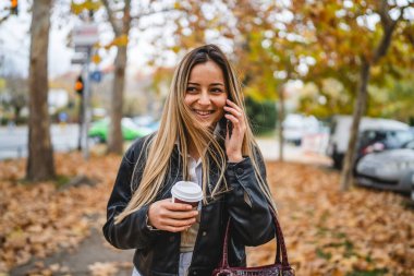 Sonbahar günü genç bir beyaz kadın şehrin kaldırımında yürüyor telefonla konuşuyor gülümsüyor elinde kahveyle gülüyor gerçek insanlar uzayı kopyalıyor.