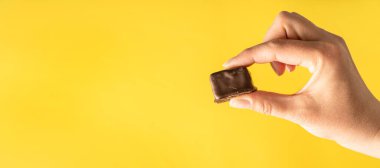 Elinde sarı arkaplan fotokopi alanının üzerinde kahverengi çikolata küpü tutan kimliği belirsiz beyaz bir kadın var.