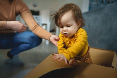 Evdeki karton kutuda annesinin yanında oynayan küçük beyaz bir kız.