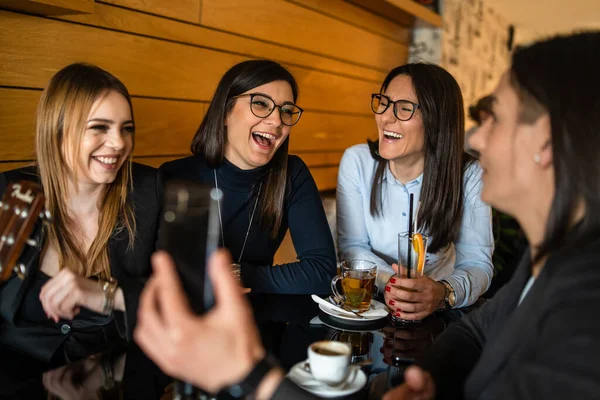 カフェやレストランに千年前からの友人たちとスマホでビデオ通話をしたり 自撮り写真を撮ったりしている最中に携帯電話を持っている若い女性が大人の白人女性グループのフロントビュー — ストック写真