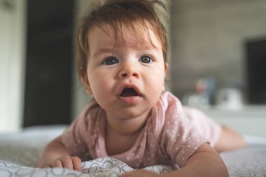 Ön manzara, beyaz, küçük bir kız bebeğini yakın çekimde yatağın üzerine uzanmış, karnını eğip gün içinde kameraya bakıyor.