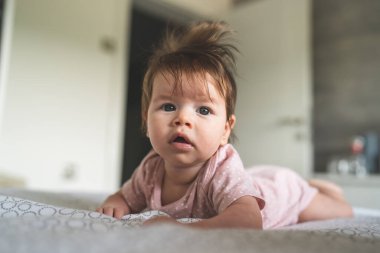 Ön manzara, beyaz, küçük bir kız bebeğini yakın çekimde yatağın üzerine uzanmış, karnını eğip gün içinde kameraya bakıyor.