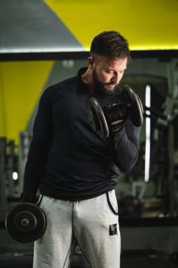 Beyaz erkek erkek sporcunun spor salonunda antreman yaparken ön manzara portresi. Koyu renk gömlekli, siyah saçlı, sakallı, ağırlık kaldıran vücut geliştirici.