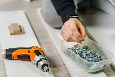 Bilinmeyen bir beyaz adamın elinde elektrikli tornavida tutarken, direktifler doğrultusunda kontrplak vidalarının mobilyalarını monte ederken, orta kısmına yaklaş - DIY konsepti kopyalama alanı