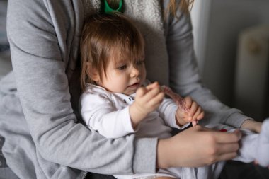 Küçük beyaz bir bebek giyiniyor. Genç bir kadın, küçük kızını kucağına alıp üstünü değiştiriyor. Gerçek insanlar, aile içi bakım ve ebeveynlik kavramı.