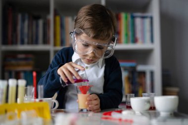 Beş yaşında, koruyucu gözlüklü beyaz bir bilim adamı masada oturmuş kimya ekipmanları oyuncaklarıyla oynuyor deney öncesi öğrenme ve eğitim konsepti ön görüşüyle oynuyor.