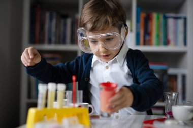 Beş yaşında, koruyucu gözlüklü beyaz bir bilim adamı masada oturmuş kimya ekipmanları oyuncaklarıyla oynuyor deney öncesi öğrenme ve eğitim konsepti ön görüşüyle oynuyor.