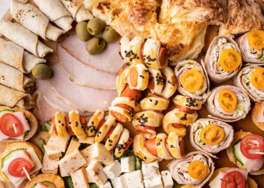 Peynir ve jambon rulolarını ahşap tabakta kapayın. Yemeye hazır çeşitli yemekler var. Aperatif masada.