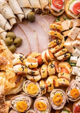 Peynir ve jambon rulolarını ahşap tabakta kapayın. Yemeye hazır çeşitli yemekler var. Aperatif masada.