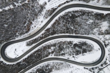 Sırbistan 'ın Knjazevac kenti yakınlarında kış günü beyaz karla kaplı dağ sırasındaki ağaçlar ve ormanlar boyunca kıvrımlı yılan yolundaki yüksek açılı hava aracı görüntüsü - Seyahat yolculuğu konsepti