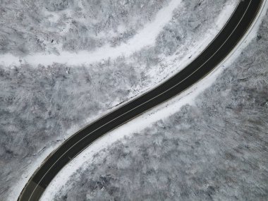High angle aerial view drone image on the curved road trough the trees and forest in mountain range with white snow in winter day near Knjazevac in Serbia - Travel journey vacation concept