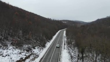 Seyahat yolculuğu ve tatil konsepti Sırbistan 'ın Knjazevac kenti yakınlarında kış günü beyaz karla dağlık alanda giden kıvrımlı serpentin yol aracının yüksek açılı hava aracı videosu