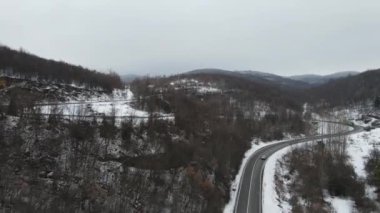 Seyahat yolculuğu ve tatil konsepti Sırbistan 'ın Knjazevac kenti yakınlarında kış günü beyaz karla dağlık alanda giden kıvrımlı serpentin yol aracının yüksek açılı hava aracı videosu