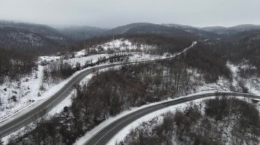 Seyahat yolculuğu ve tatil konsepti Sırbistan 'ın Knjazevac kenti yakınlarında kış günü beyaz karla dağlık alanda giden kıvrımlı serpentin yol aracının yüksek açılı hava aracı videosu