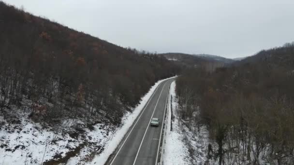 旅行の旅と休暇のコンセプトセルビアのKnjazevac近くの冬の日に白い雪と山の範囲で運転サーペンタイン道路の車の曲線上の高角度の空中ビュードローンビデオ — ストック動画