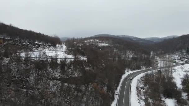 旅行の旅と休暇のコンセプトセルビアのKnjazevac近くの冬の日に白い雪と山の範囲で運転サーペンタイン道路の車の曲線上の高角度の空中ビュードローンビデオ — ストック動画