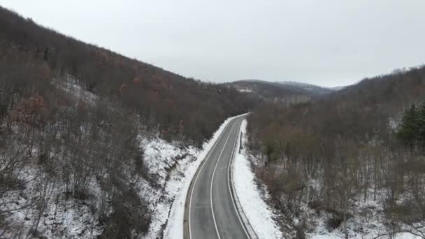 旅行の旅と休暇のコンセプトセルビアのKnjazevac近くの冬の日に白い雪と山の範囲で運転サーペンタイン道路の車の曲線上の高角度の空中ビュードローンビデオ — ストック動画