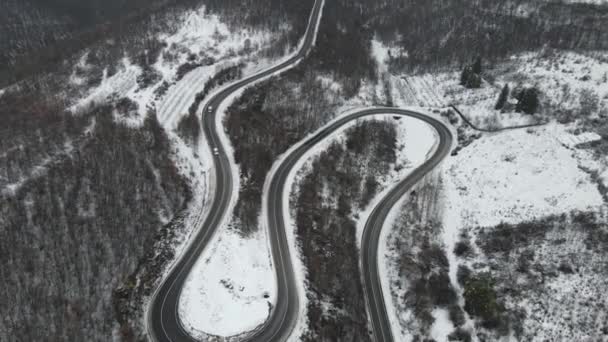 旅行の旅と休暇のコンセプトセルビアのKnjazevac近くの冬の日に白い雪と山の範囲で運転サーペンタイン道路の車の曲線上の高角度の空中ビュードローンビデオ — ストック動画