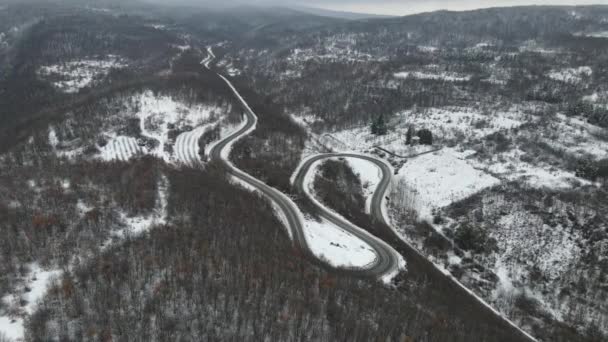 旅行の旅と休暇のコンセプトセルビアのKnjazevac近くの冬の日に白い雪と山の範囲で運転サーペンタイン道路の車の曲線上の高角度の空中ビュードローンビデオ — ストック動画