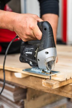 Close up on hand of unknown carpenter working with an electric jigsaw cutting wood with saw woodworking hobby concept