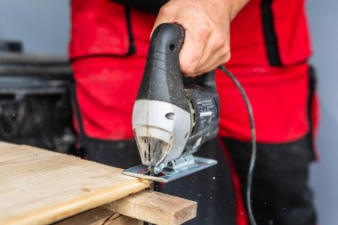 Close up on hand of unknown carpenter working with an electric jigsaw cutting wood with saw woodworking hobby concept