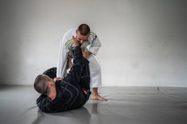 İki Brezilyalı jiu jitsu bjj figörleri dövüş sanatları eğitimi erkek atlet tekniği ya da tatami minderinde siyah beyaz kimono gi üniforması giyerek yedek olmak.