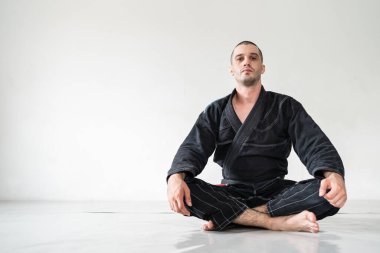 Yetişkin erkek atlet Bjj Brezilyalı jiu jistu siyah kuşak beyaz duvarın önünde kimono gi 'nin içinde fotokopi alanı ile kameraya bakıyor.