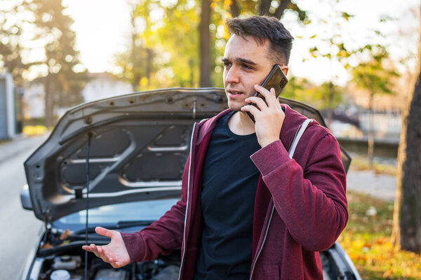 Один взрослый кавказский мужчина стоял у своего автомобиля с открытым капотом и сломанным двигателем, держа в руках буксировочную службу для помощи на дороге концепцию помощи на дороге осенью