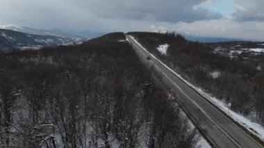 Seyahat yolculuğu ve tatil konsepti. Sırbistan 'ın Knjazevac kenti yakınlarında kış günü beyaz karla dağlık alanda giden otomobil üzerindeki yüksek açılı hava aracı videosu.