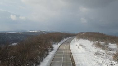 Seyahat yolculuğu ve tatil konsepti. Sırbistan 'ın Knjazevac kenti yakınlarında kış günü beyaz karla dağlık alanda giden otomobil üzerindeki yüksek açılı hava aracı videosu.