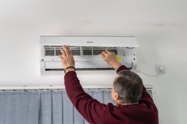 Beyaz bir adamın, evdeki havalandırmayı tamir ederken, filtreyi çıkarırken ya da yerine koyarken arka plan görüntüsü.