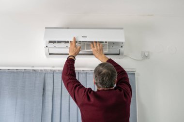 Beyaz bir adamın, evdeki havalandırmayı tamir ederken, filtreyi çıkarırken ya da yerine koyarken arka plan görüntüsü.