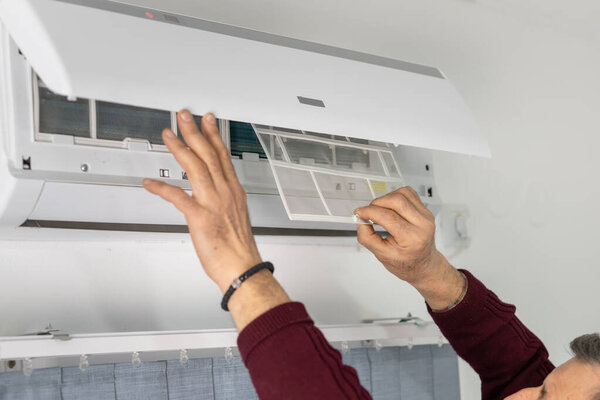 Задний вид на руки одного старшего кавказца, который чистит кондиционер в доме, меняя фильтр