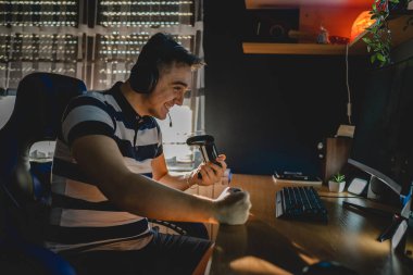 Kafkasyalı genç bir erkek, karanlık odada bilgisayarında video oyunu oynuyor. Kulaklıkları masada zaferi kutluyor. Ya da mağlubiyetten bıkmış.