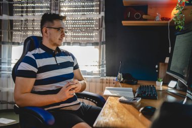 Masada oturan beyaz bir gencin masaüstü bilgisayarının monitörüne bakması kripto döviz kurunu analiz etmesi yatırımını izlemesi veya gerçek insanları satması.